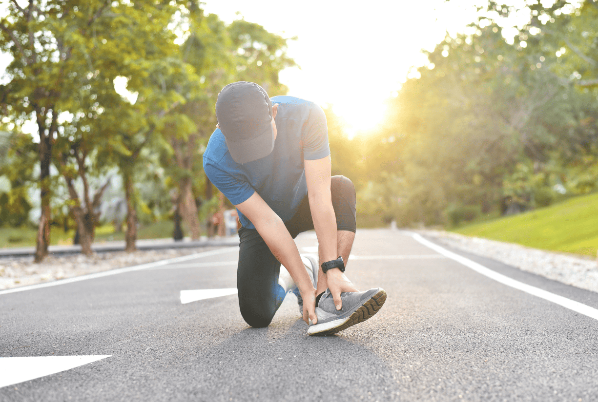 man on running path outside taking off shoe to examine foot or lower leg