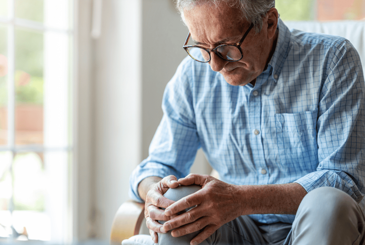 senior person wearing glasses holding knee at home
