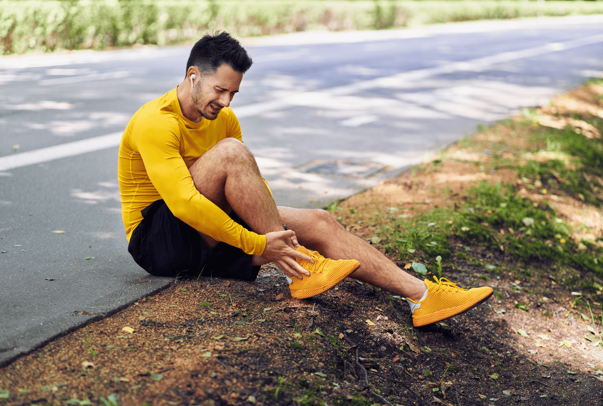 man sitting down on side of running path holding ankle