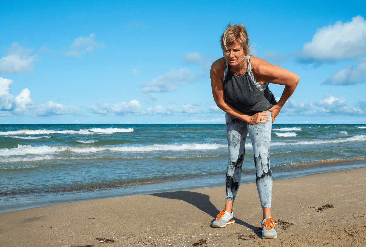 woman at beach hunched over holding hip in pain