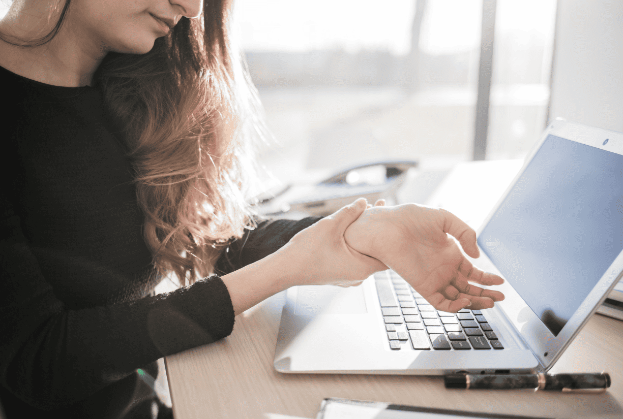 woman at desk with laptop examining wrists in discomfort