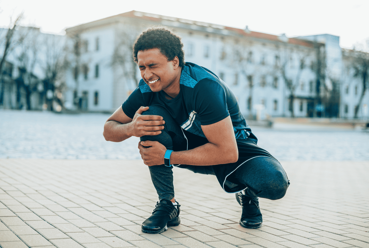 man outside in athletic outfit holding knee in pain