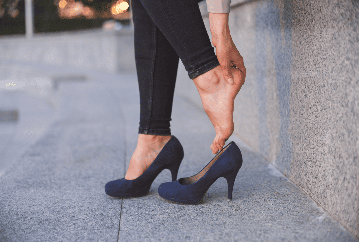 woman outside with one high-heel on and the other off holding heel of foot