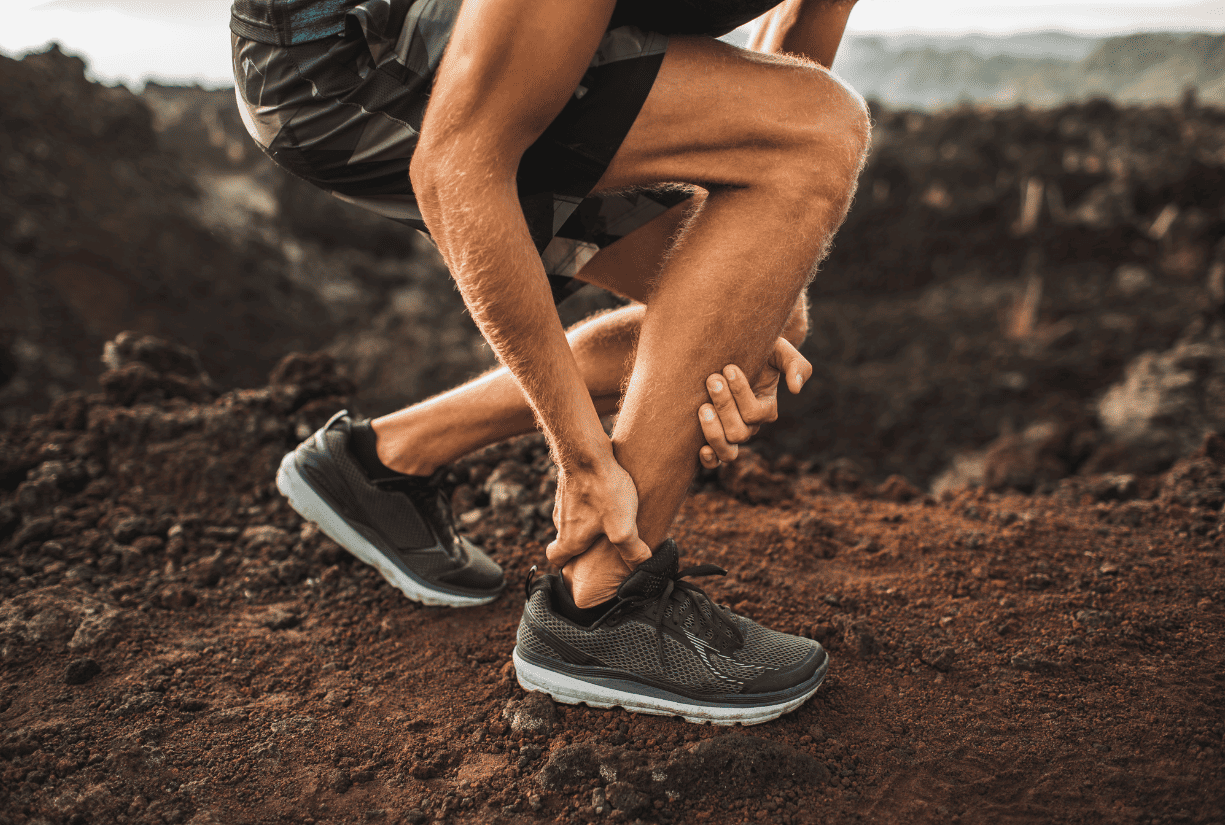 man in the middle of hiking hunched over holding lower leg in pain