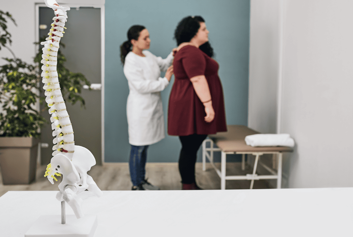 Woman give spinal inspection on female patient in the backdrop of a spinal chord model