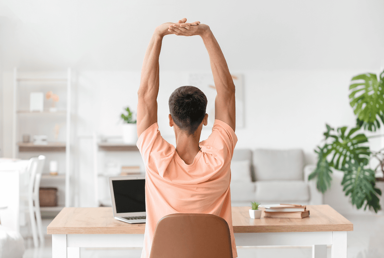 Man sitting at home desk stretching with arms aboves arms